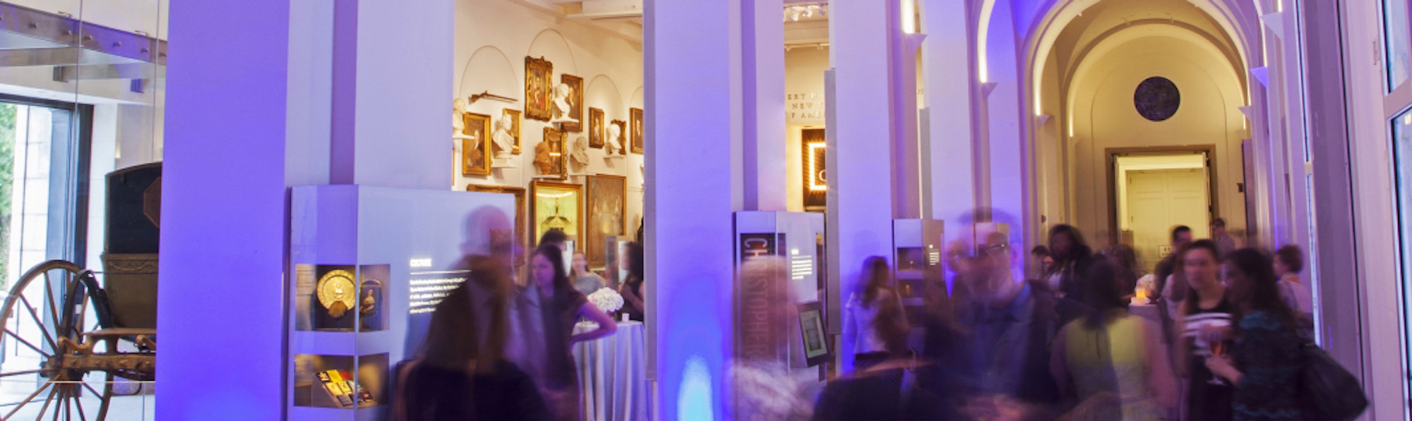 Blurred crowd of people under gallery archways lit in purple light