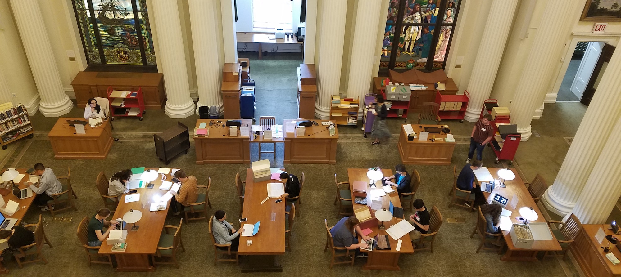an overhead shot of the library's reading room showing multiple researchers at the tables with computers and papers laid out.