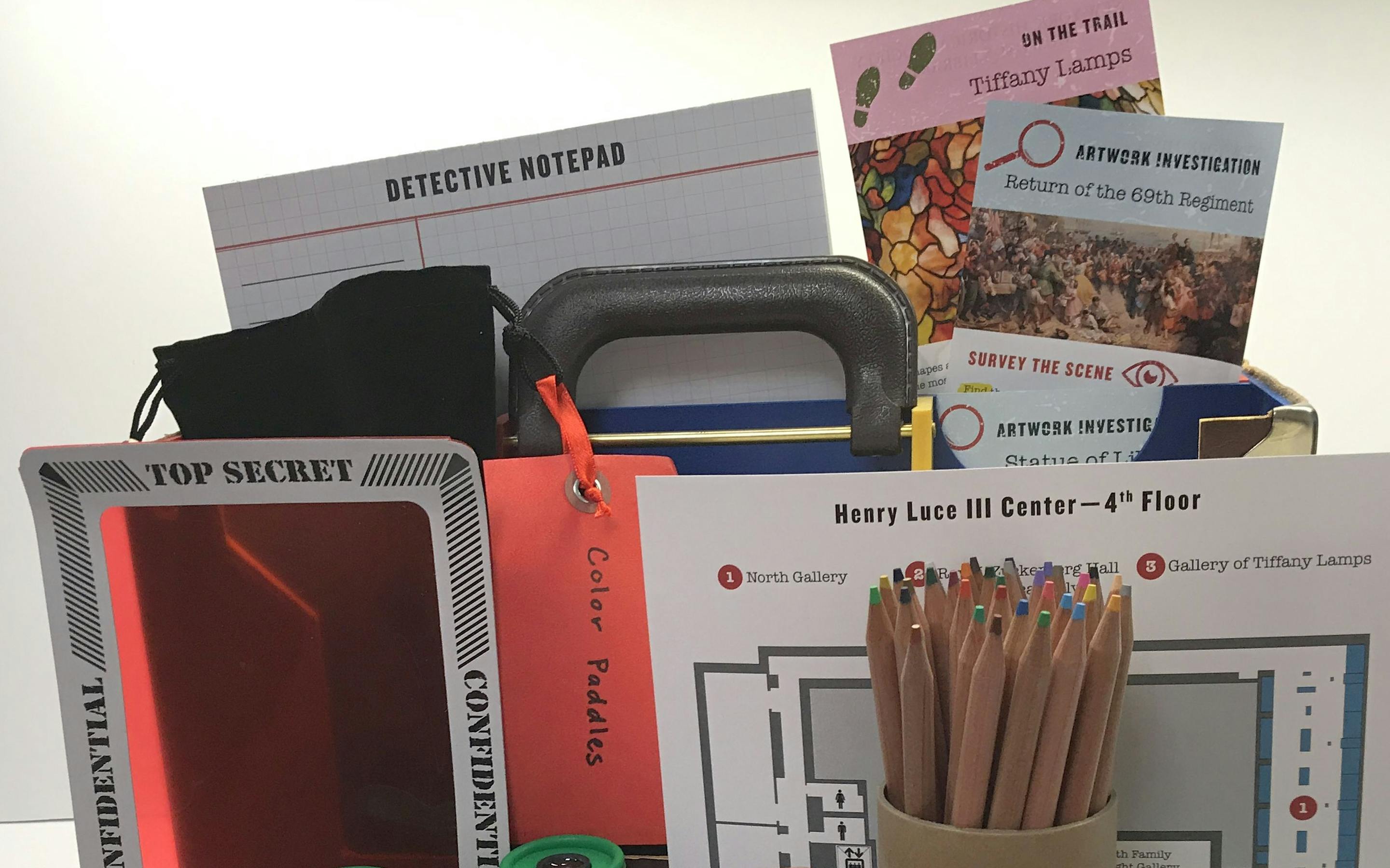 photo of the history detective briefcase with activities shown outside including colored pencils, binoculars, and notepads