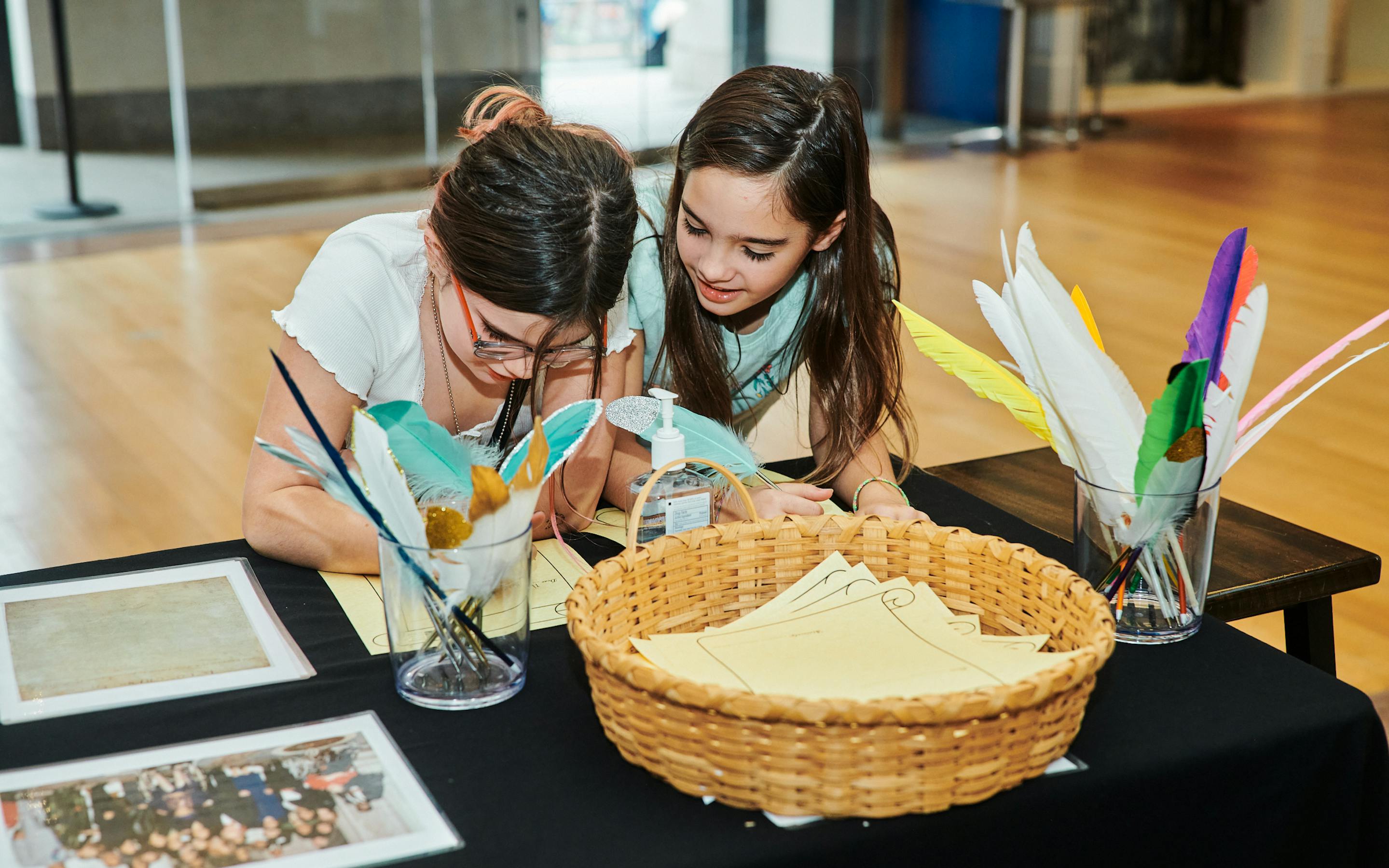 two girls do a craft at a table in the museum