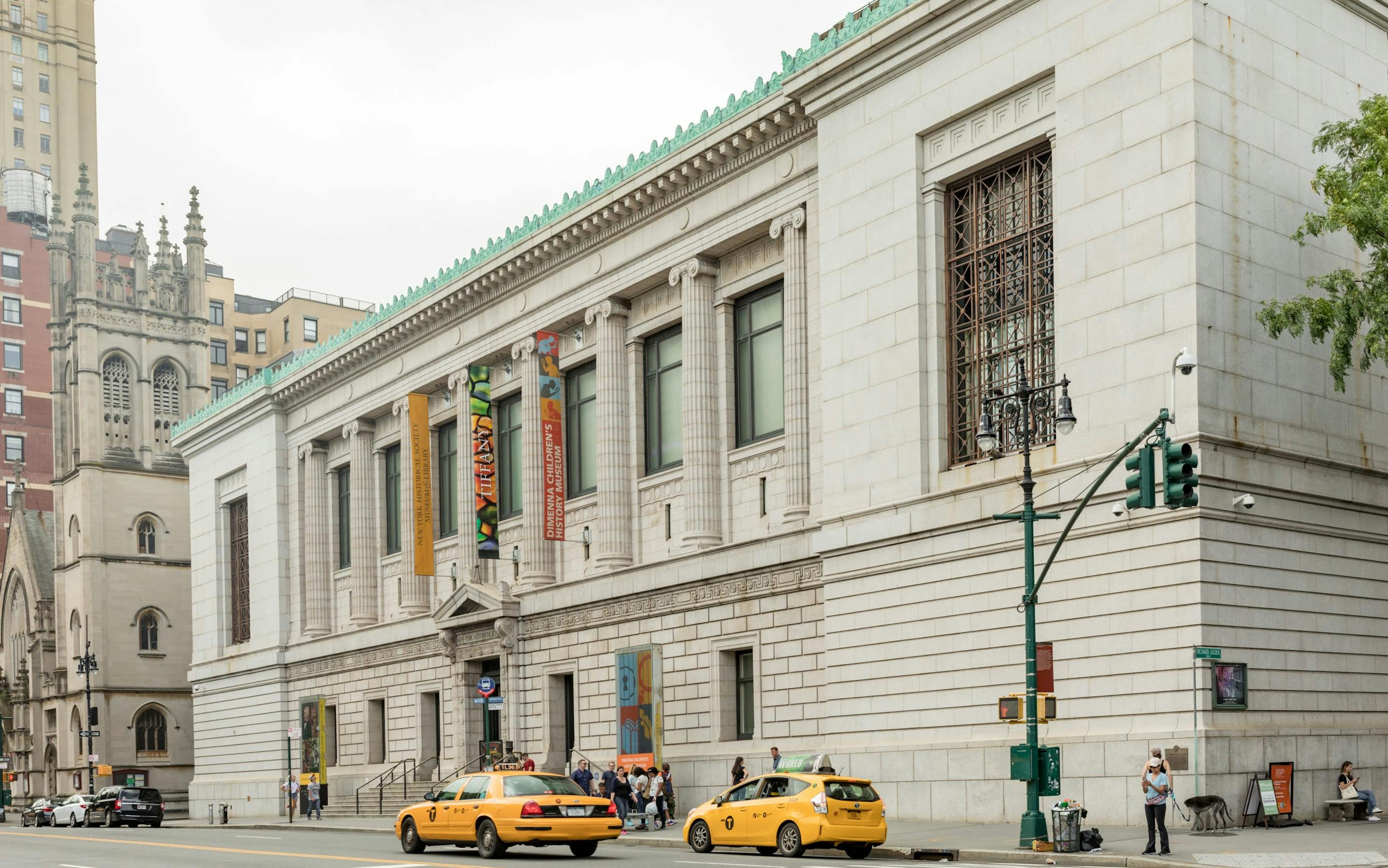 The New-York Historical facade during the day with cabs passing by and people crowded outside