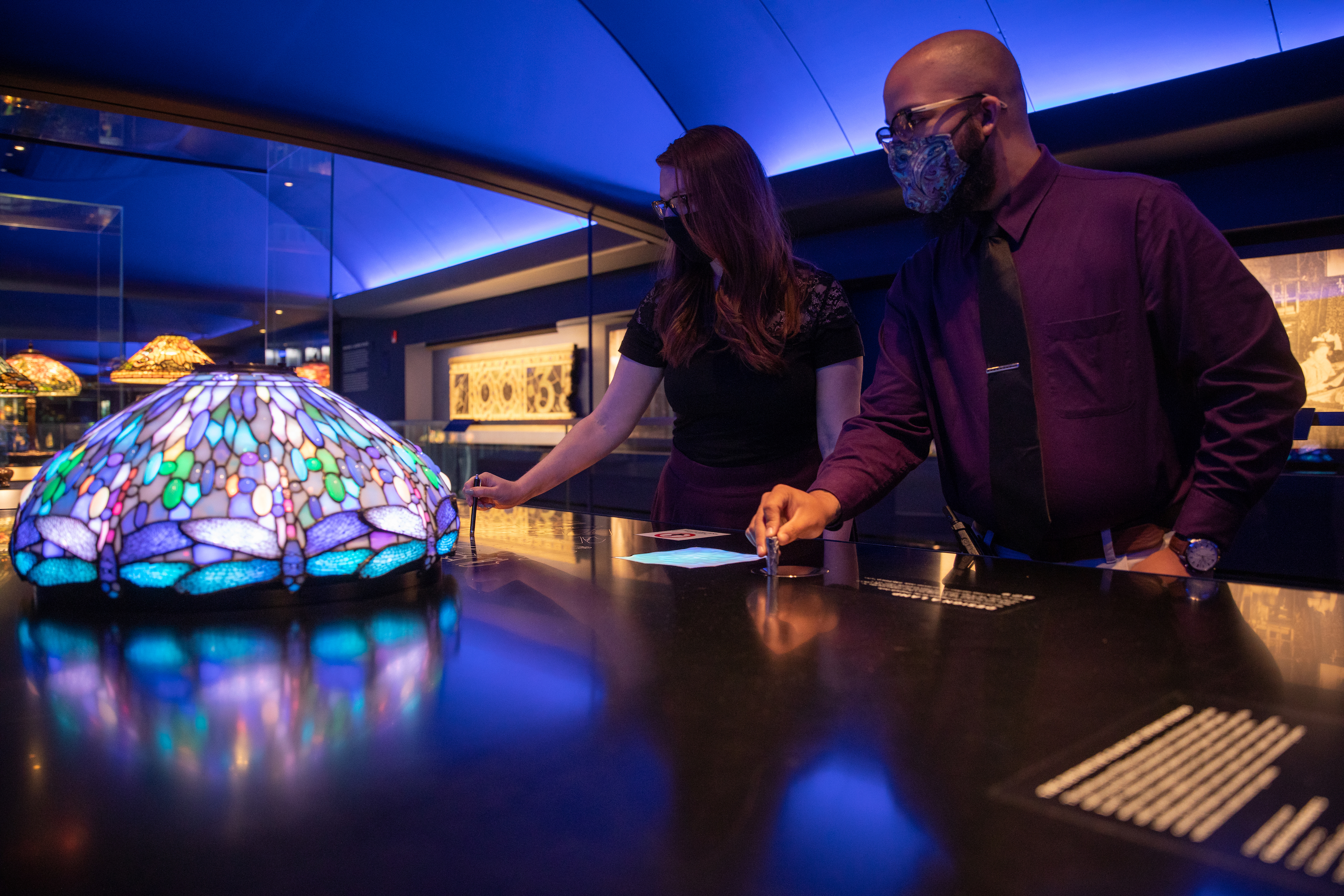 two masked visitors in the Gallery of Tiffany lamps play with an interactive