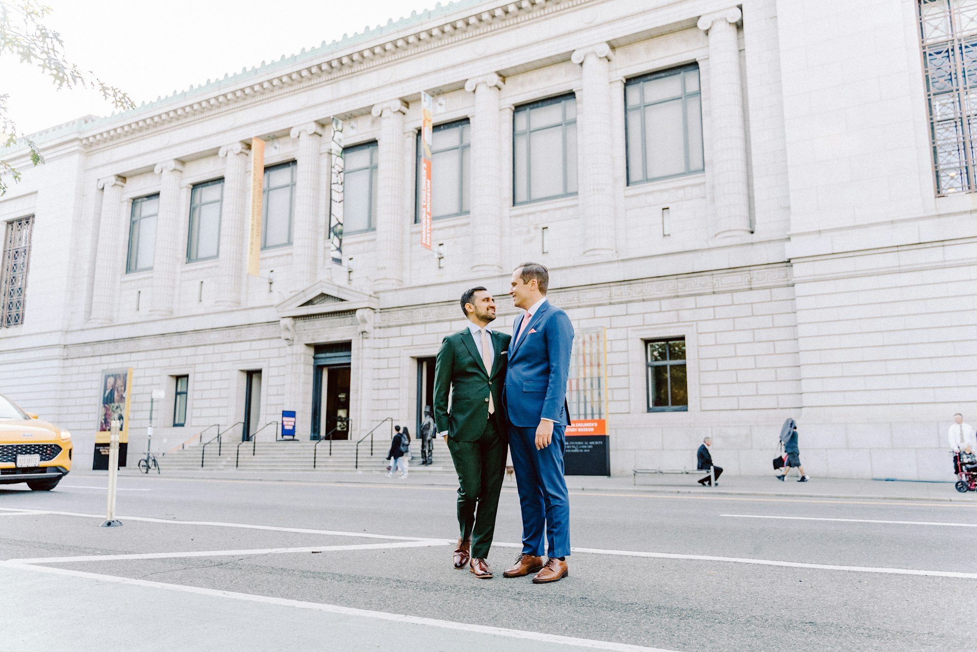 a gay male couple in suits posing in front of the Museum on central park west