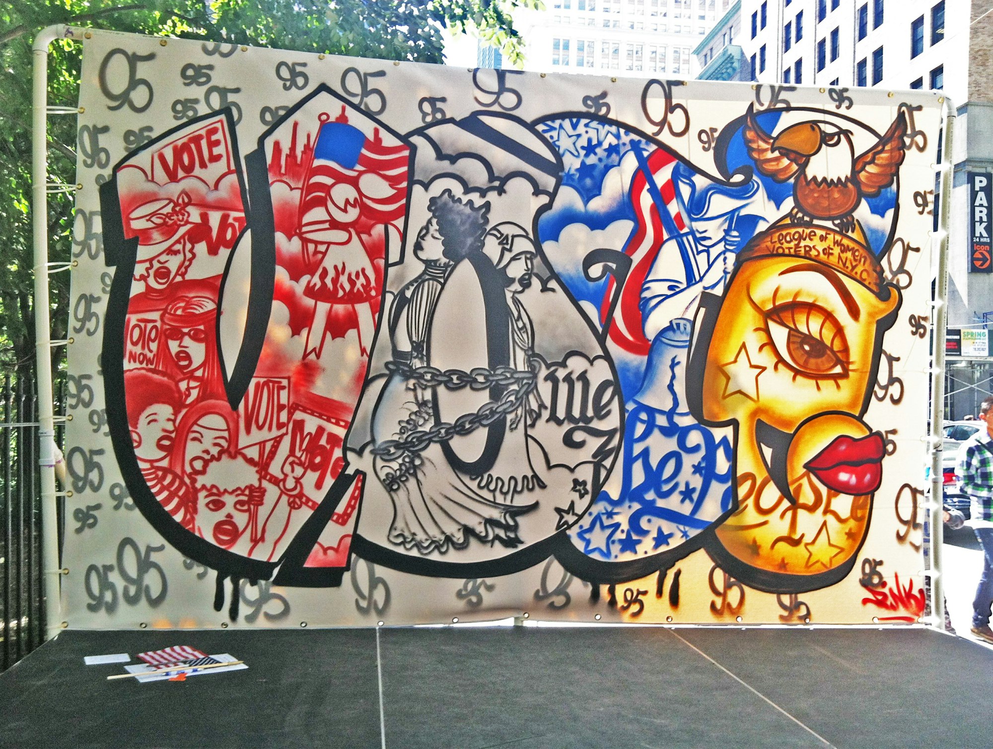 an image of Lady Pink's colorful VOTE mural outside on the day it was created, in red, white, blue, and gold colors showing such motifs as an eagle, a protest, suffragists, and revolutionary war soldiers.