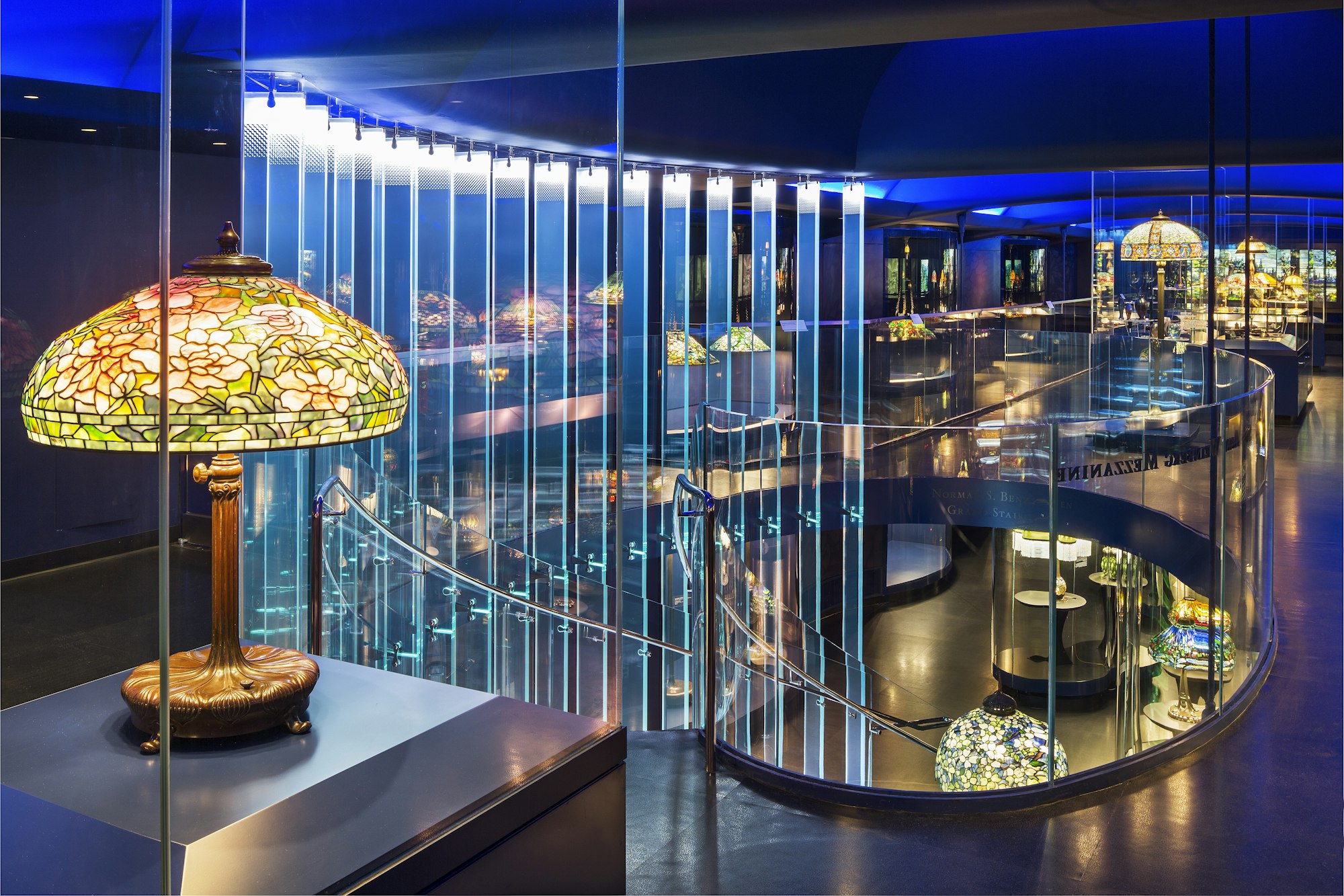 a view inside the gallery of tiffany lamps showing the staircase and mezzanine, all lit up in blue light