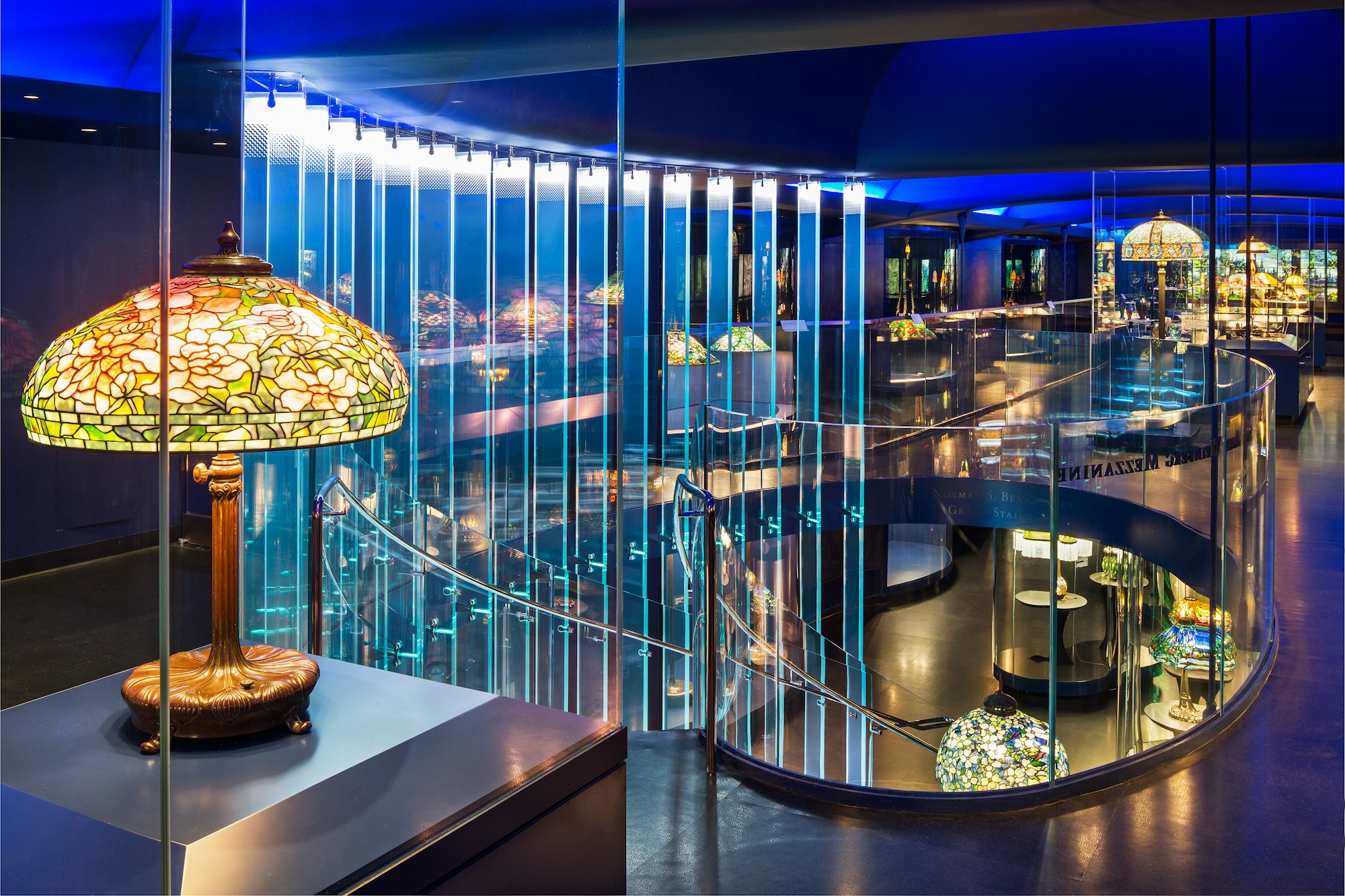 a view inside the gallery of tiffany lamps showing the staircase and mezzanine, all lit up in blue light