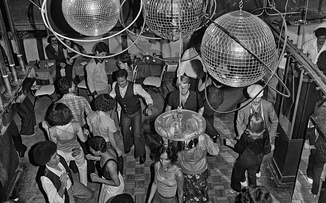 black and white image of a crowded dance floor at a disco in 1979 with multiple couples of various races dancing and several sparkling disco balls hanging from the ceiling
Bill Bernstein, Reflections, 40 East 58th Street, 1979. Photograph (c) Bill Bernstein