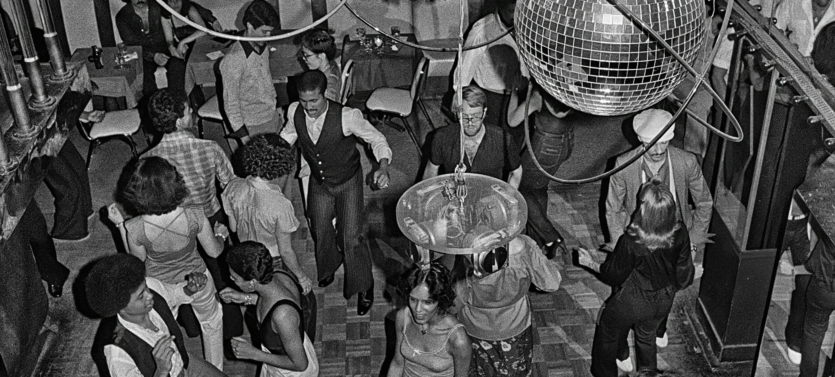 black and white image of a crowded dance floor at a disco in 1979 with multiple couples of various races dancing and several sparkling disco balls hanging from the ceiling
Bill Bernstein, Reflections, 40 East 58th Street, 1979. Photograph (c) Bill Bernstein