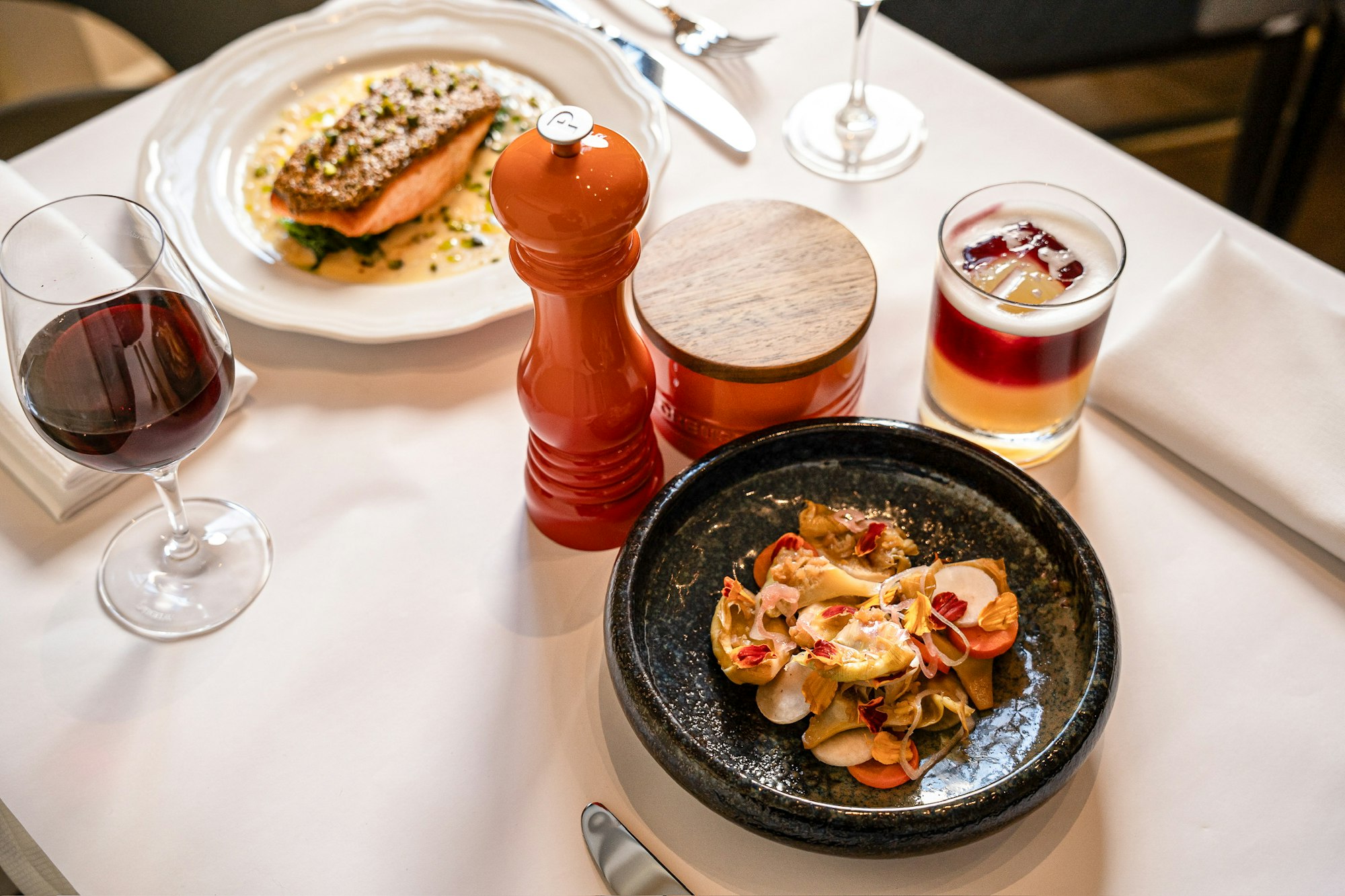 a white table cloth in Clara with two plates of food and a glass of red wine and a cocktail.