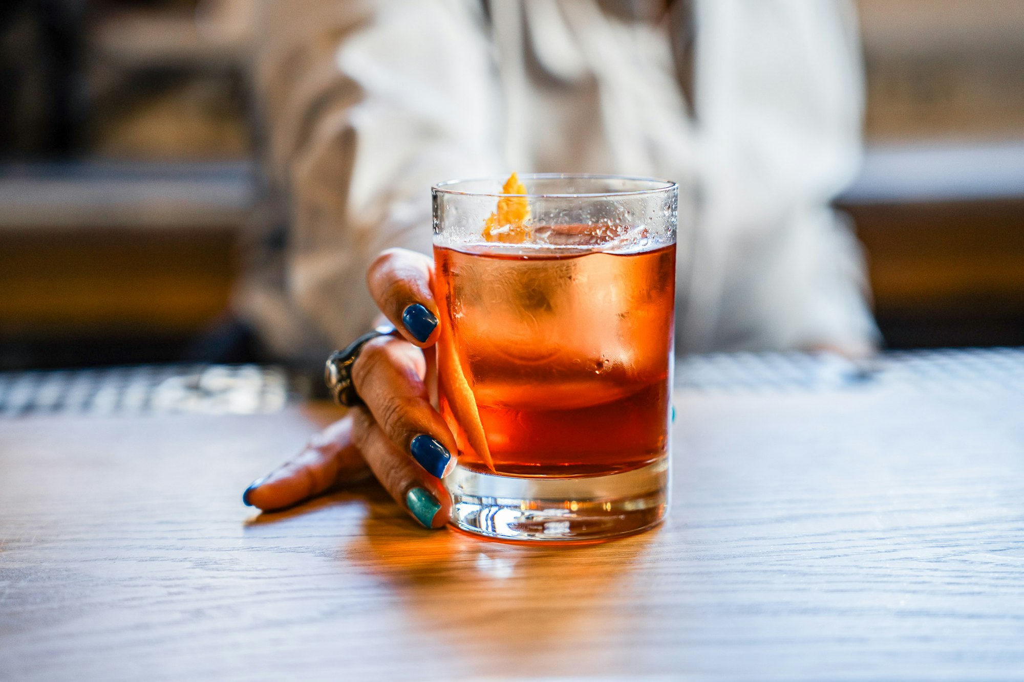 a cocktail with a hand picking it up on the bar in Clara