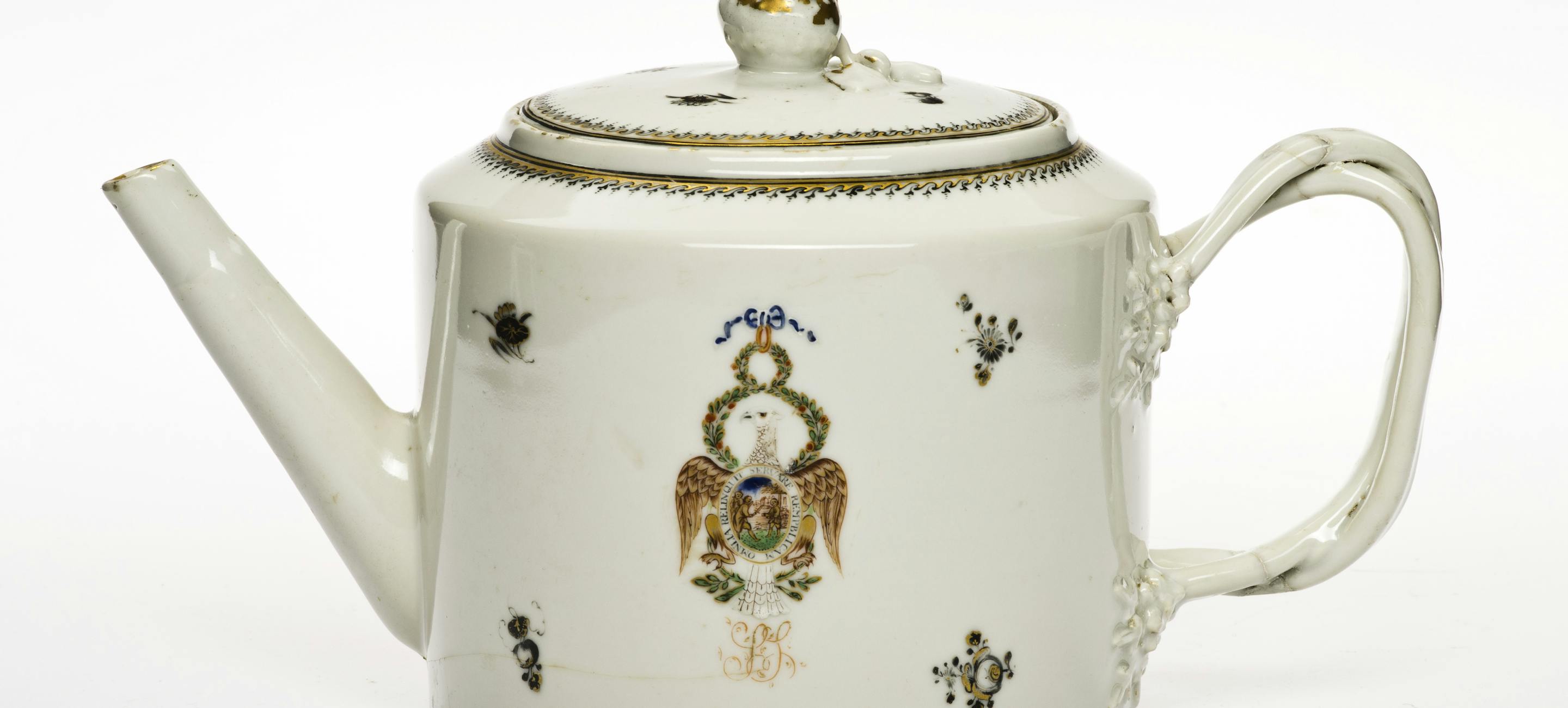 a white porcelain teapot with a straight spout, a handle and some light designs on the front
