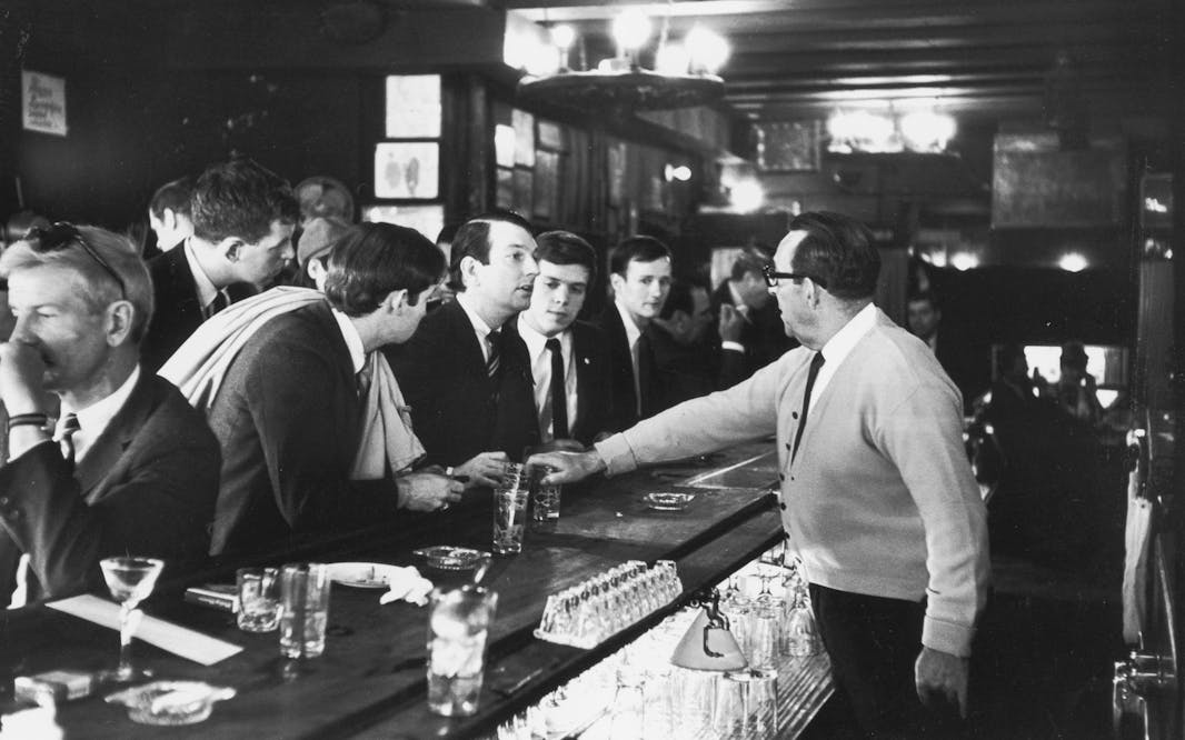 a crowd of men stand at the bar in NYC and talk to the bartender, part of a sip-in at Julius' Bar in 1966
