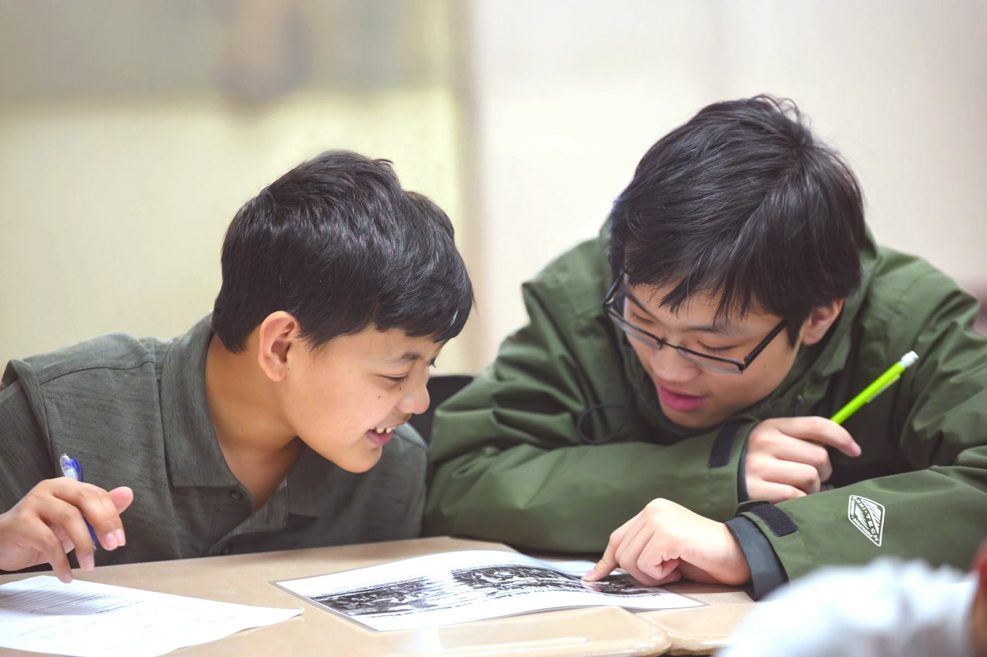 two young boys sit at a table over schoolwork looking engaged and excited.