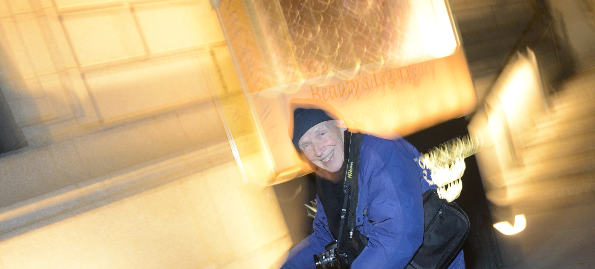 Bill Cunningham on his bicycle smiling as he's pedaling at night.