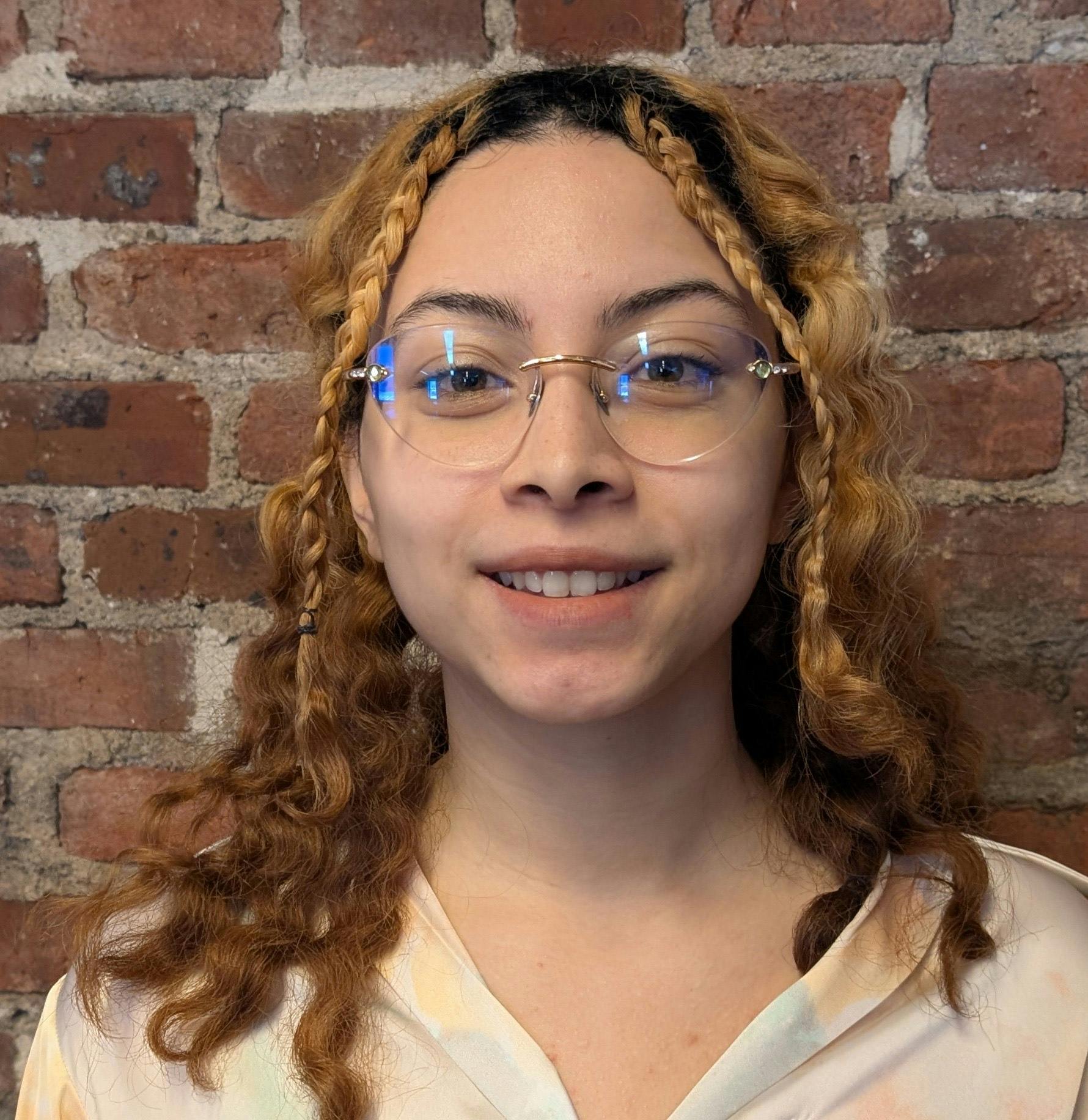 Photograph of a woman smiling, standing in front of a brick wall.