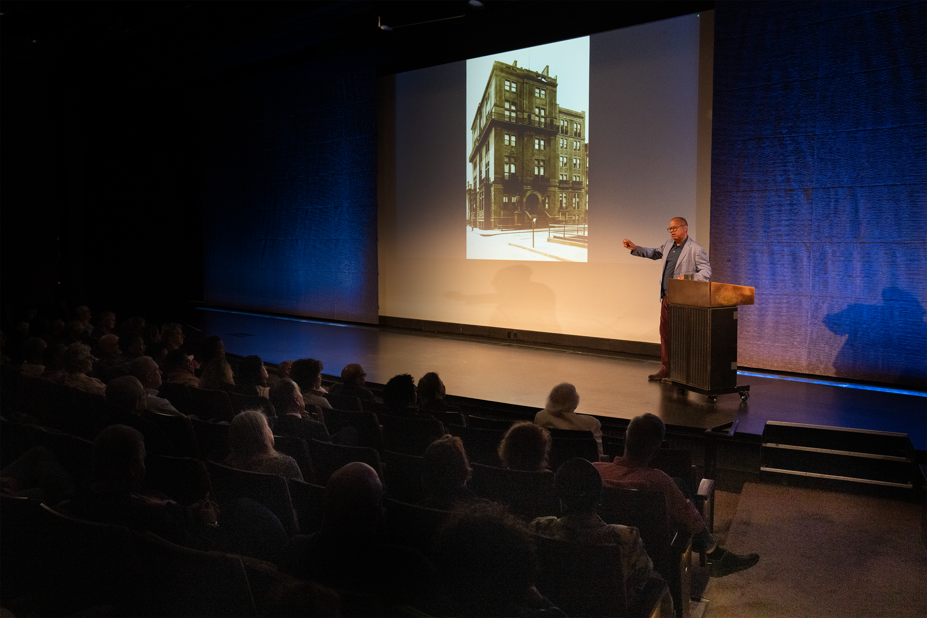 a lecturer in the auditorium pointing to an image on the screen