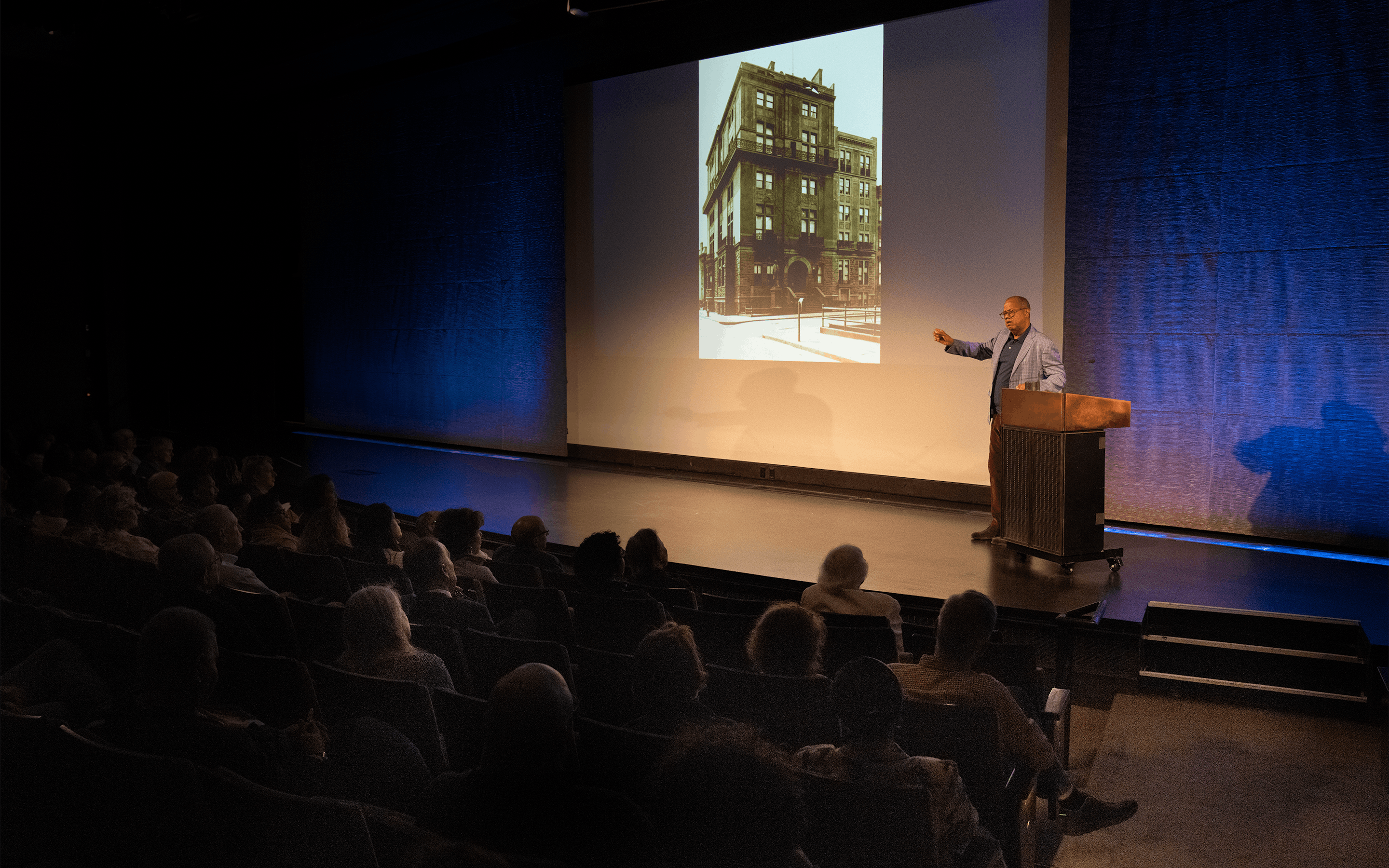 a lecturer in the auditorium pointing to an image on the screen