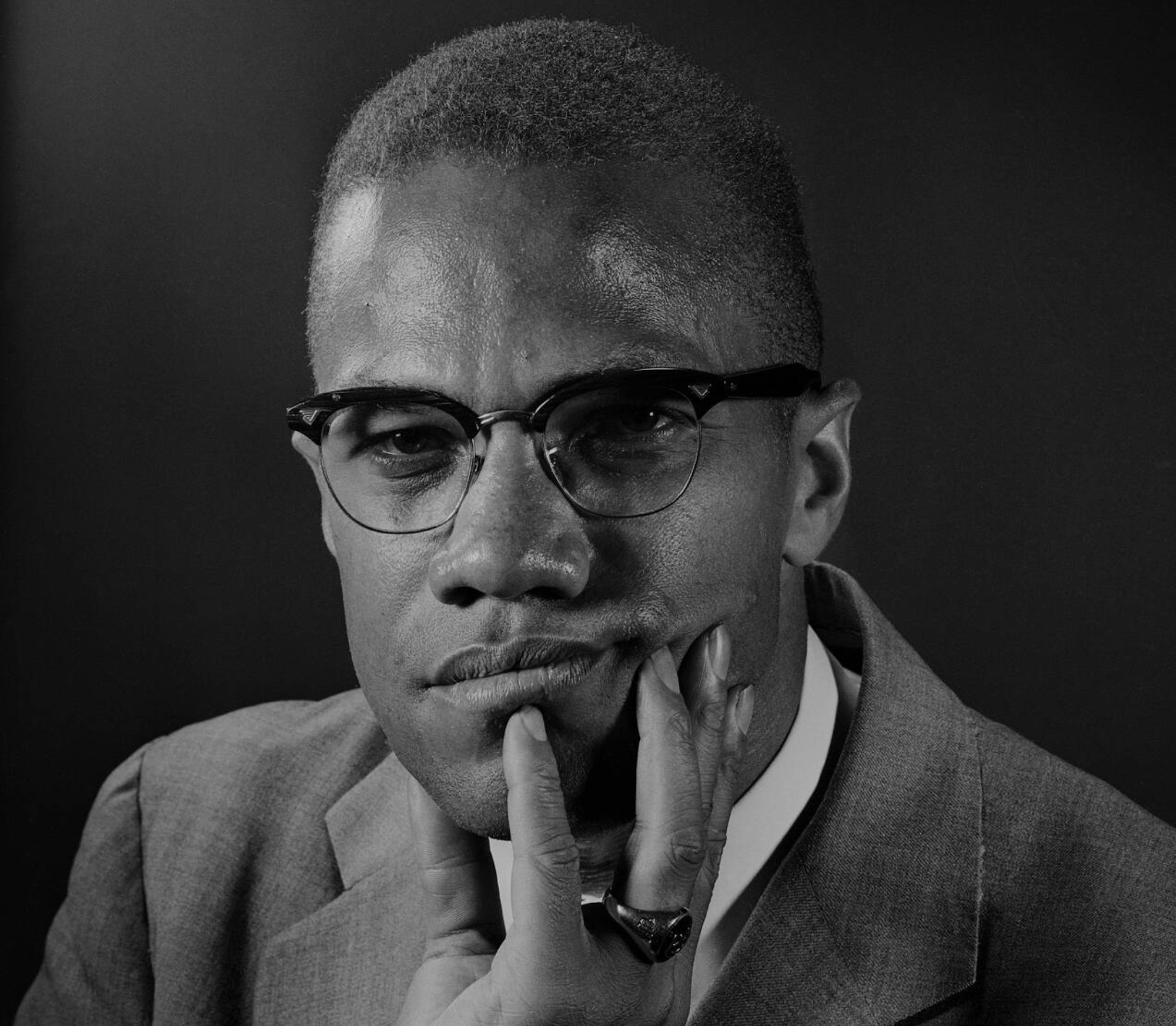 a 1964 press photo of Malcolm X resting his chin on his hand. By Eddie Adams - Wirephoto copy, Public Domain,