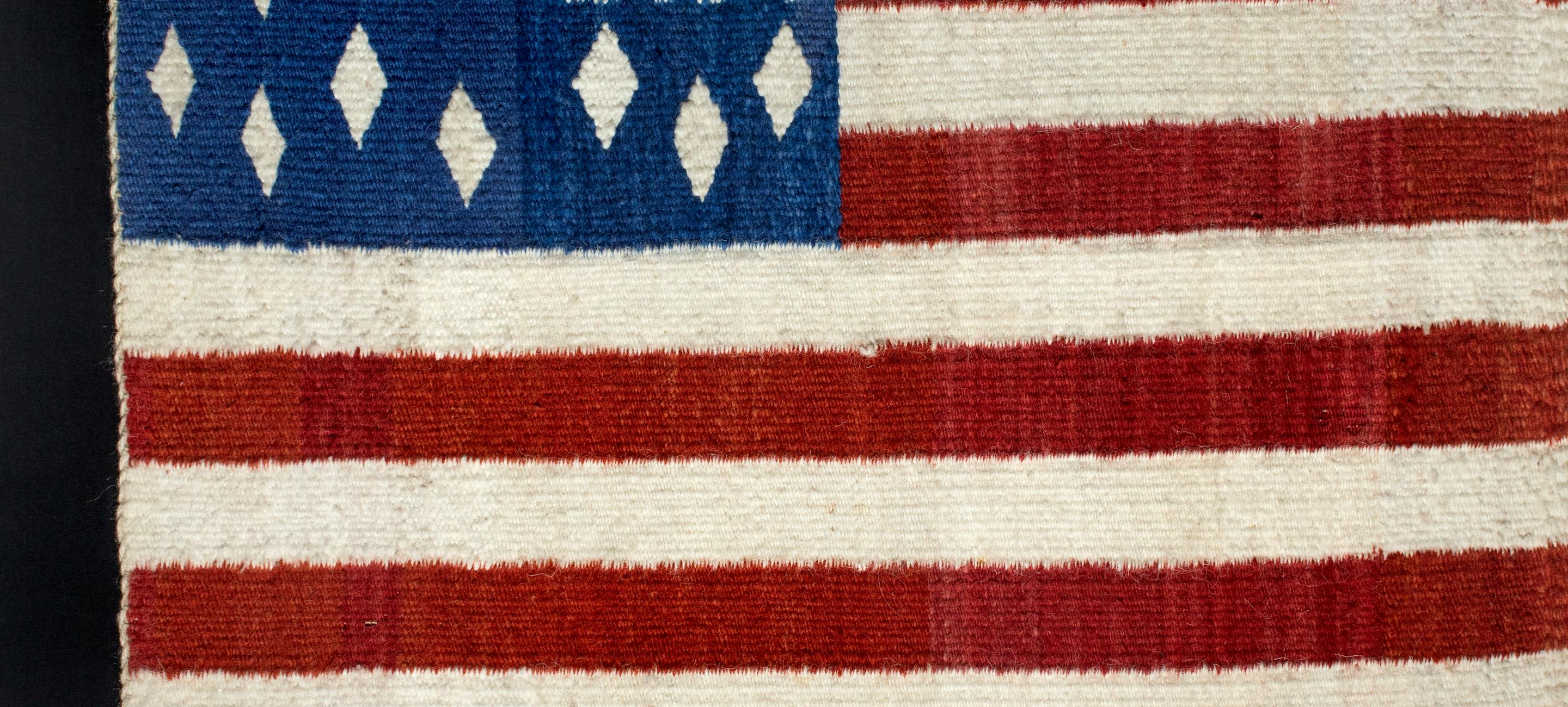 A woven American flag with a "USA" in the blue field and diamonds instead of stars. Diné Weaver, USA flag, late 19th century. Handspun wool, vegetal and native dyes. The New York Historical, Promised gift of Agnes Hsu-Tang and Oscar Tang, The Hsu-Tang Collection