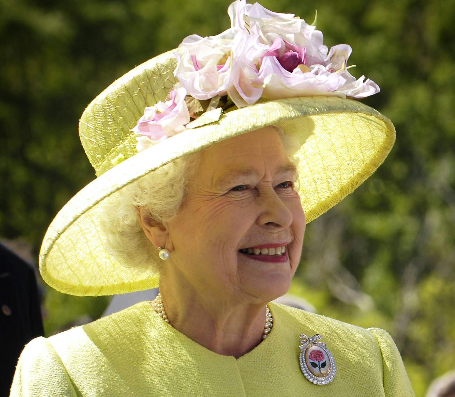 Queen Elizabeth smiles while wearing a bright yellow dress and hat with pink flowers. Her Majesty the Queen, aged 81, of the United Kingdom. Photo taken during a visit in NASA’s Goddard Space Flight Center. Greenbelt, Maryland, USA.