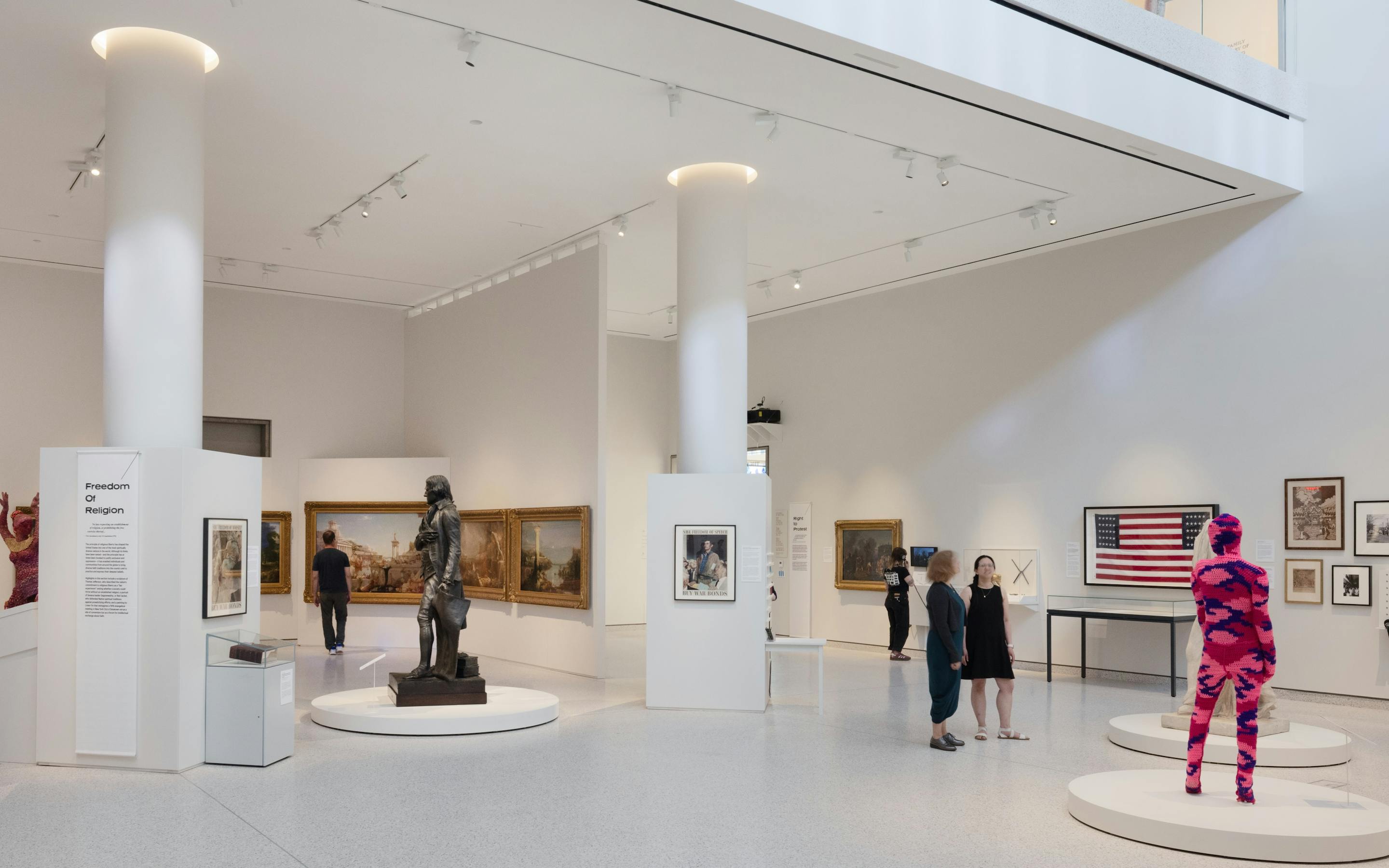 The interior of Klingenstein Family Gallery with art and sculpture for Democracy Matters visible and visitors walking around. Photo by Bridgit Beyer
