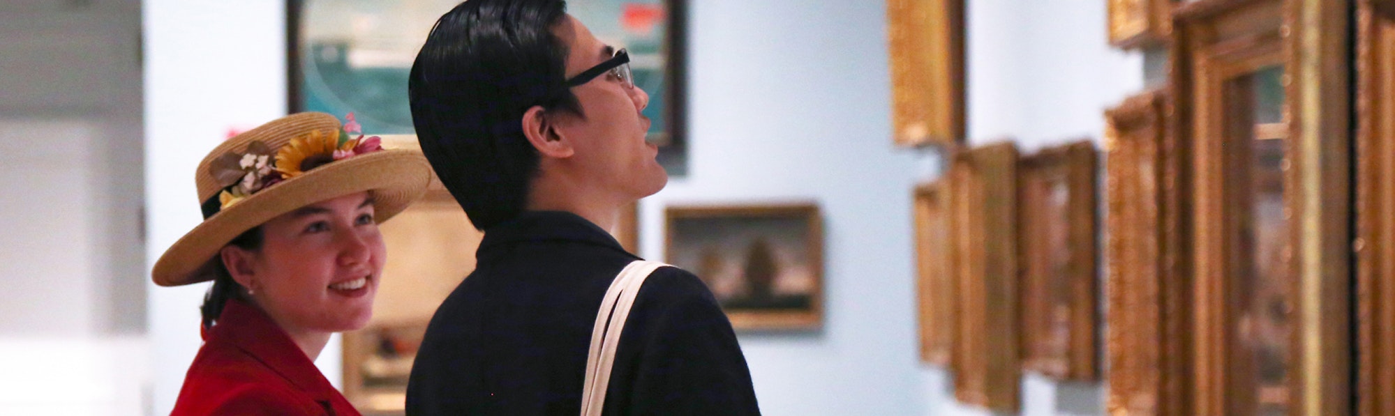 two museum visitors looking a gallery wall of framed artwork
