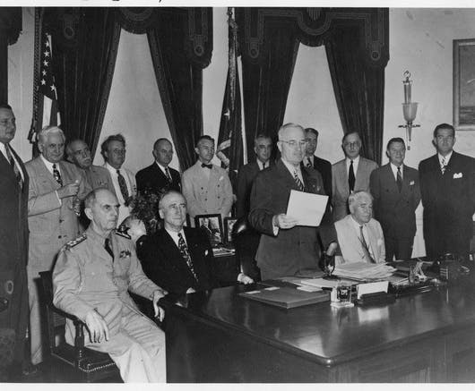 President Harry Truman reads the Japanese surrender message, which effectively ends World War II, surrounded by members of his Cabinet and others, August 14, 1945.