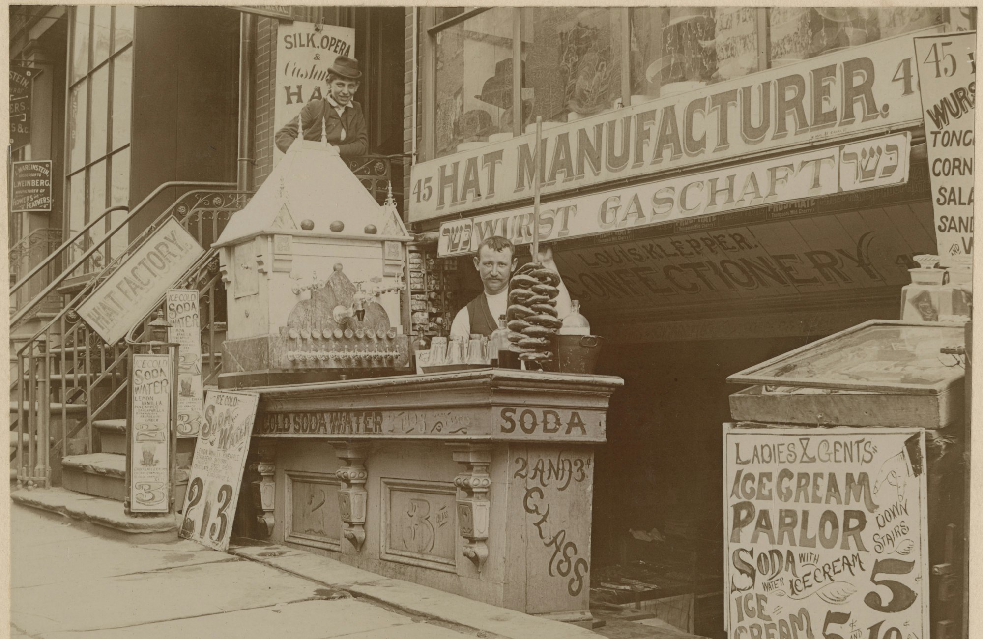 A black and white photo circa 1900 of Louis Klepper Confectionary and Sausage Manufacturers, 45 E. Houston Street, New York, featuring a man standing at his storefront with a selection of sausages