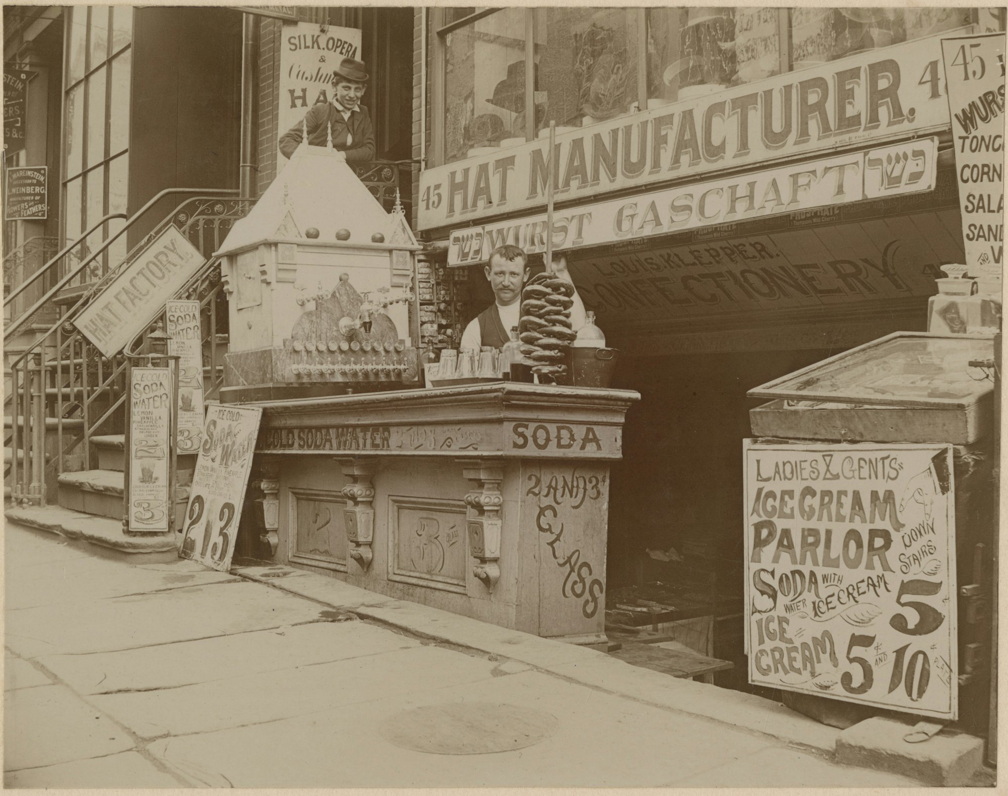 A black and white photo circa 1900 of Louis Klepper Confectionary and Sausage Manufacturers, 45 E. Houston Street, New York, featuring a man standing at his storefront with a selection of sausages