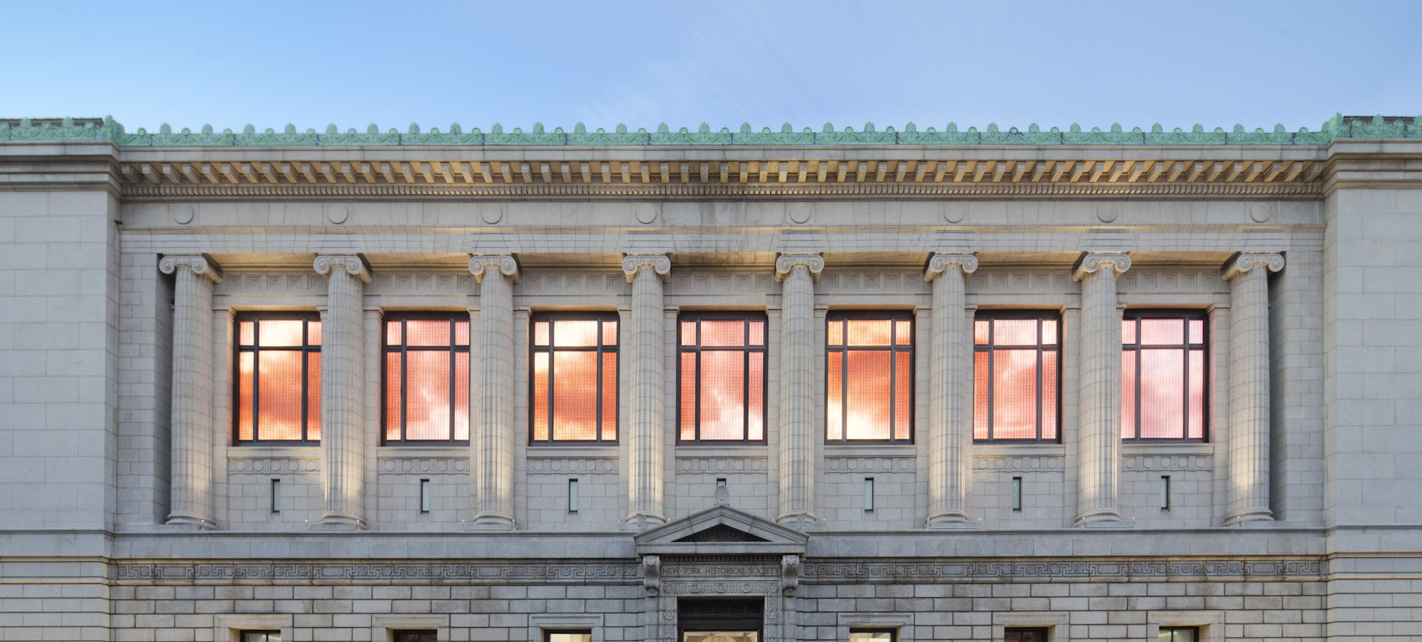 facade of the new-york historical society with the windows lit up in orange