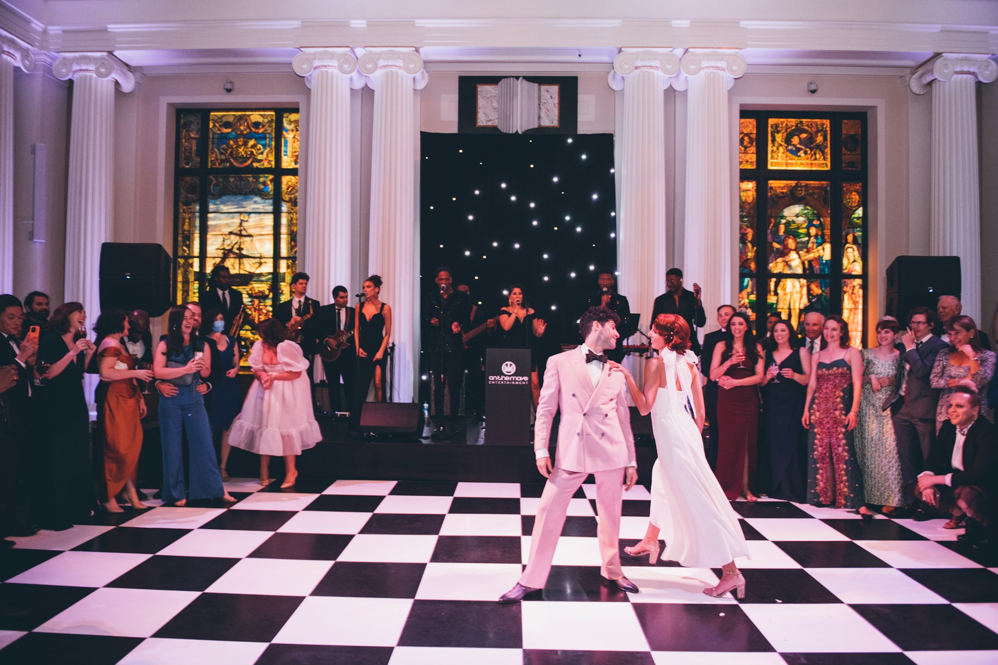 a wedding reception in the library with a couple dancing on a black and white checked floor.