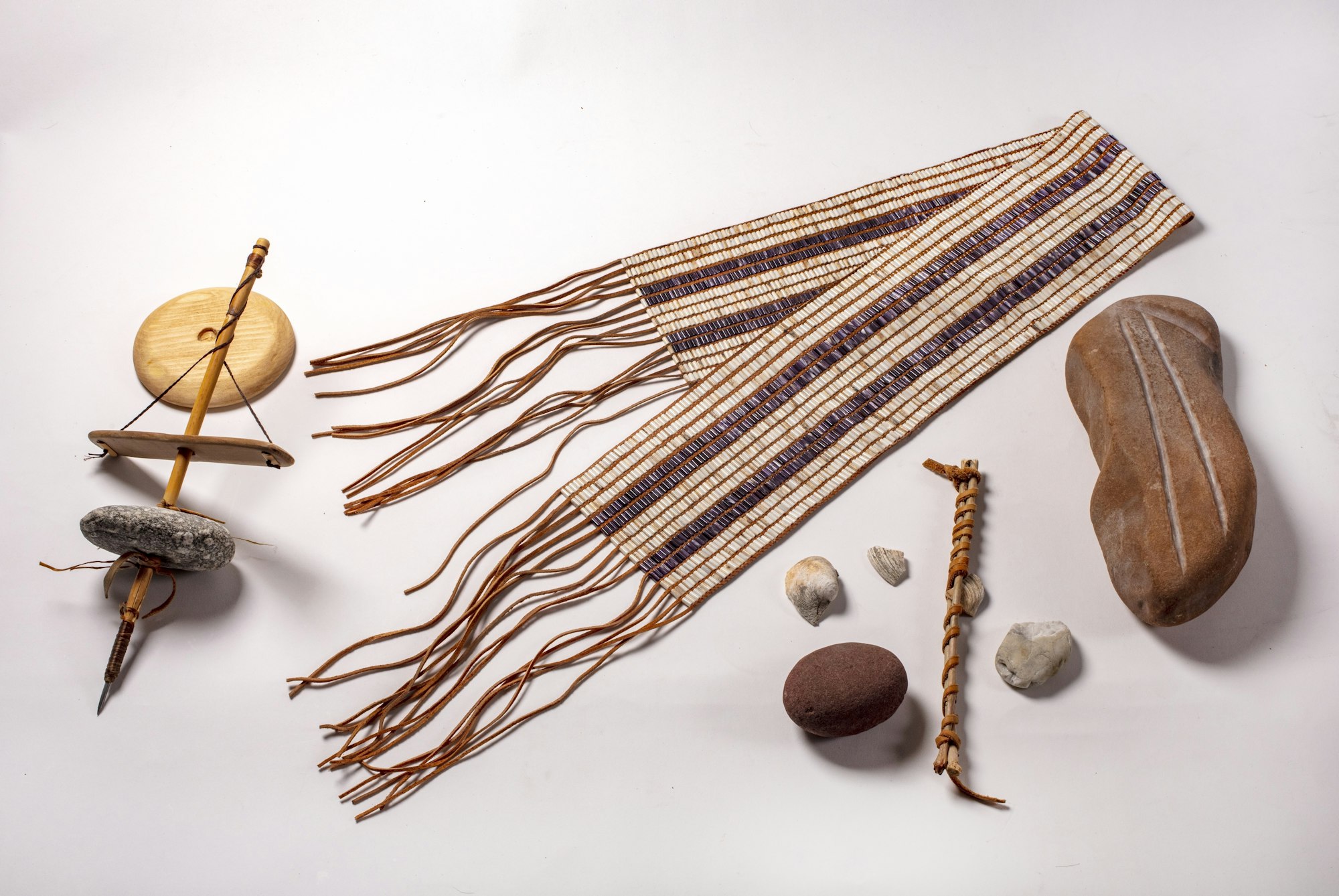 a two-row wampum belt folded in half displayed next to Native tools made of stone and wood.