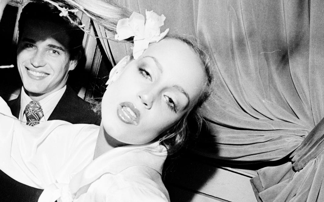 A Bil cunningham photo from 1975 showing Jerry Hall and a male guest at the St Regis Pink Ball, with Jerry posing for the camera and holding her long ponytail aloft.
Bill Cunningham. Jerry Hall at St. Regis Pink Ball, February 22, 1975